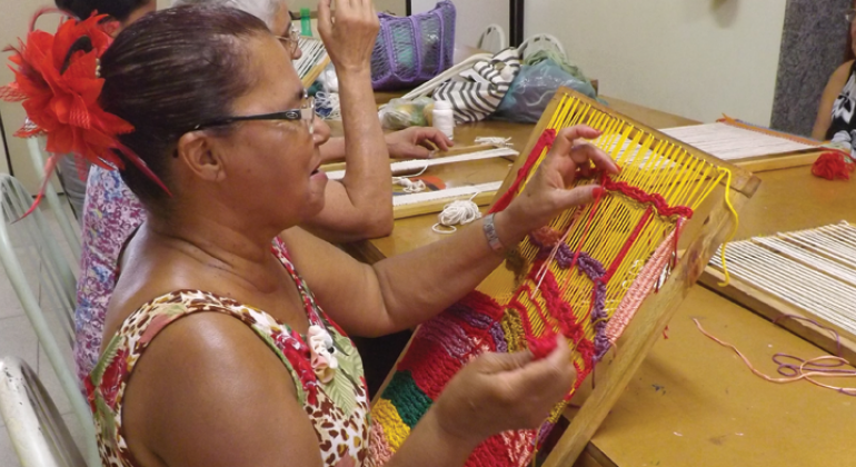 Mulher faz tecelagem com linhas coloridas em tear. 