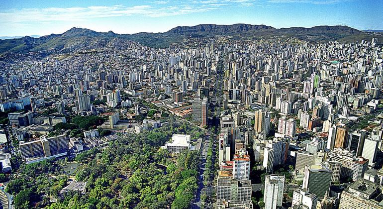 Vista aérea de BH, no centro, a avenida Afonso Pena, à esquerda, à frente, o Parque Municipal e ao fundo, a Serra do Curral e o céu. 