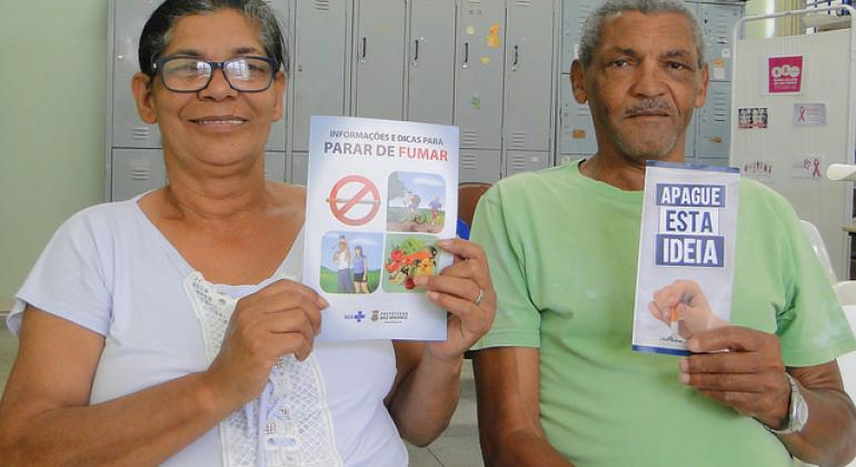Homem e mulher, participantes do programa contra o tabagismo, segurando folhetos informativos e educativos distribuídos pelos centros de saúde.