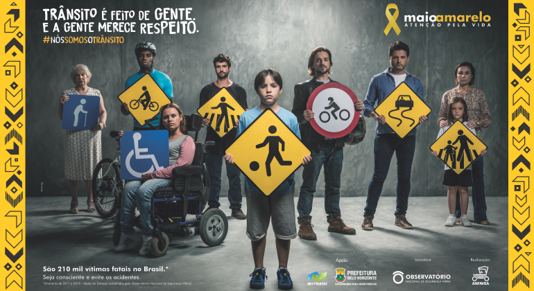 Imagem de de nove pessoas de difetentes idades com placas de trânsito correspondentes às atividades que exercem ou o que são: jogador de futebol, pedestre, ciclista, cadeirnte ou idoso, por exemplo. 