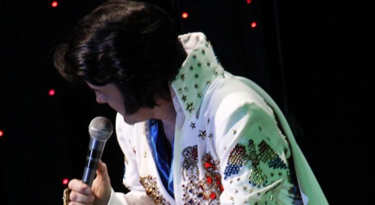 Cover de Elvis Presley cantando ao microfone. 