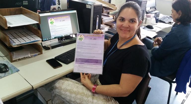 Guia rápido sobre hanseníase é disponibilizado aos profissionais dos centros de saúde para agilizar o diagnóstico da doença. Foto: Leila Porto Mulher, sentada em mesa de computador, mostra Guia rápido sobre hanseníase.