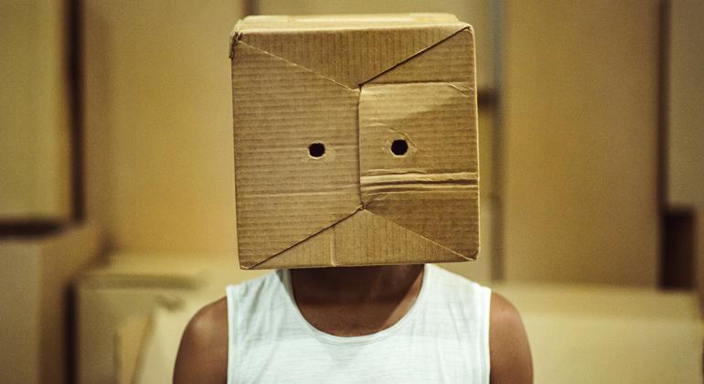 Teatro Chico Nunes apresenta, entre os dias 19 e 20/5, a peça "A Toque de Caixa!" Foto: Paulo Bernardo Ator negro de camiseta branca com caixa de papelão an cabeça com dois furos na altura dos olhos.