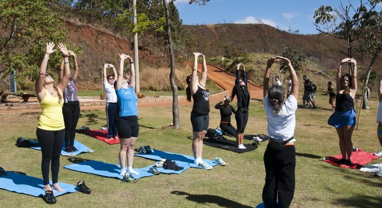 Confira os principais eventos gratuitos que acontecem em BH neste fim de semana, entre os dias 11 e 13 de maio. Foto: Divulgação PBH Mais de sete pessoas, de pé, fazem alongamento, sentadas em cime de tapetinhos, em área verde, durante o dia.