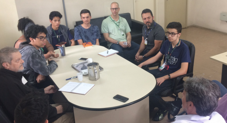 Jovens das equipes do Hackathon se reúnem com Prodabel e BHTrans. Dez pessoas estão sentadas ao redor de uma mesa. 
