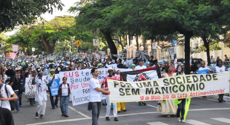 Praça da Liberdade recebe desfile da escola de Samba Liberdade Ainda que Tam Tam no Dia Nacional da Luta Antimanicomia, celebrado em 18/5. Foto: Isabel Baldoni/PBH Mais de duzentas pessoas fazem passeata em avenida em prol da Luta Manicomial, com faixas. A faixa à frente da passeata tem os dizeres: "Por uma Sociedade sem Manicômio".