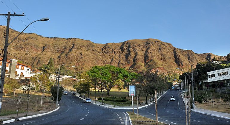 Avenida que leva ao parque dos mangabeiras com alguns carros na pista; Serra do Curral ao fundo, durante o dia. 