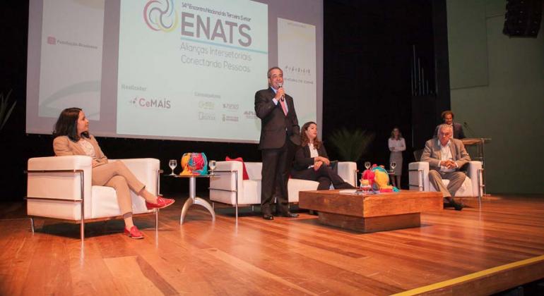 Abertura do 14º Encontro Nacional do Terceiro Setor, com dois homens e uma mulher no palco com projeção ao fundo. Da esquerda para a direita: Laís de Figueirêdo Lopes, consultora; Tomáz de Aquino Resende, procurador-geral de BH; Maíra Colares, secretária municipal de Assistência Social, Segurança Alimentar e Cidadania; e Juca Ferreira, secretário municipal de Cultura.