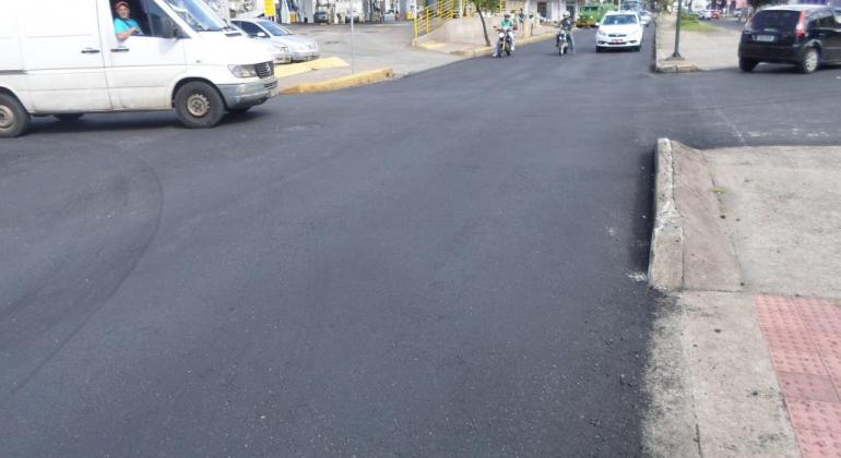 Rua recapeada, asfaltada e sem buracos após obras da prefeitura. Veículos circulando na via, próximo ao posto de combustíveis.