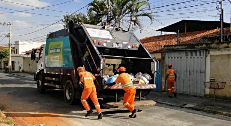 Três garis correm atrás de caminhão da Coleta domiciliar em dia de sol