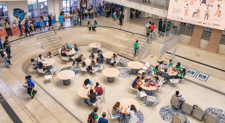 Formas de prevenção para evitar exposição ao vírus HIV e outras infecções sexualmente transmissíveis serão debatidas no CRJ no dia 29/8. Foto: Ricardo Antunes/PBH Mais de vinte jovens, sentados em dez mesas, em grupos, no espaço do Centro de Reverência da juventude; à esquerda, outras vinte pessoas estão de pé.
