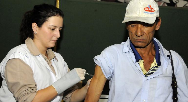 Mulher vacina um senhor em situação de rua.