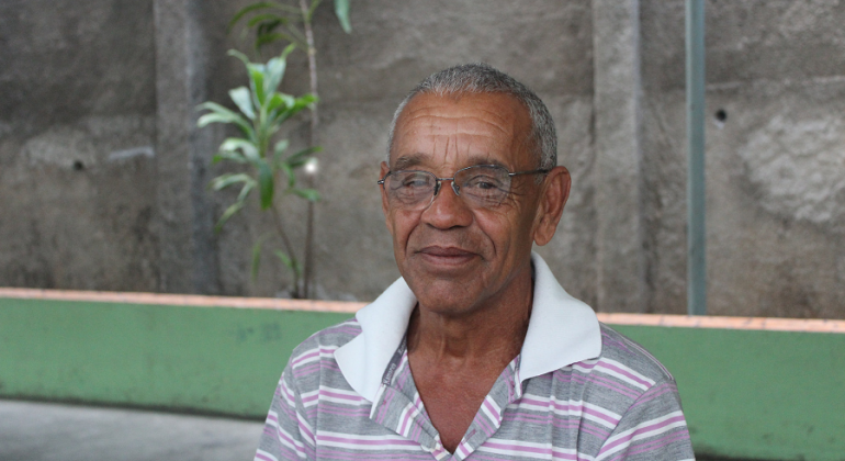 Senhor de óculos; ao fundo, um muro com uma planta. 