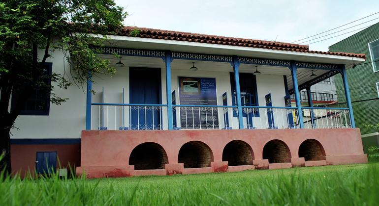 Casarão branco com portas e grade azul, durante o dia. 