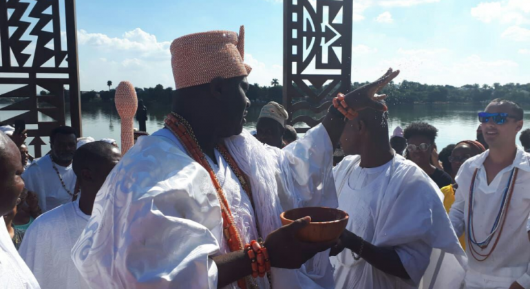 Rei da cidade nigeriana de Ifé asperge água sobre as pessoas na Pampulh. Rei usa turbante e roupa branca.