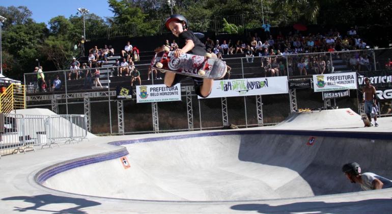 Criança dá salta de skate no ar em pista no Parque Lagoa do Nado; ao fundo, plateia acompanha. Foto de edição do evento Skate Invasion em 2017. 