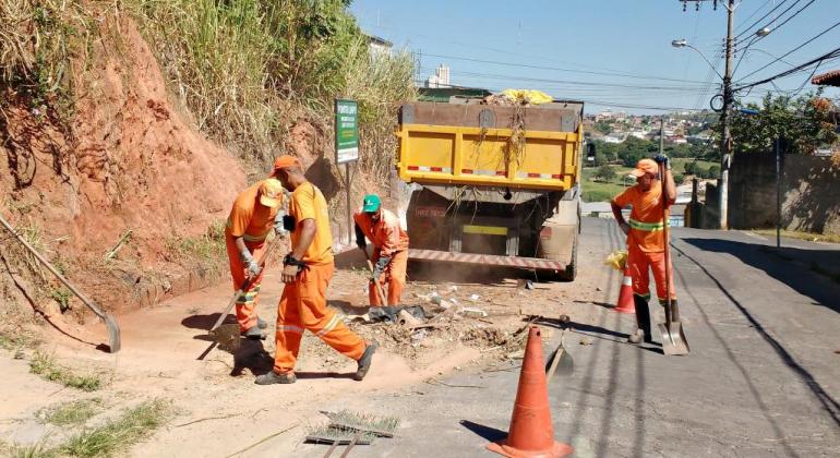 Garis varrem rua, logo atrás há um caminhão e, ao lado, uma placa com texto "ponto limpo"