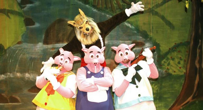 O espetáculo infantil “3 Porquinhos - O Clássico” está em cartaz no Teatro Marília de 14 a 22/7, sábados e domingos, às 16h. Foto: Divulgação Cena teatral em que Lobo Mau está atrás de três porquinhos.
