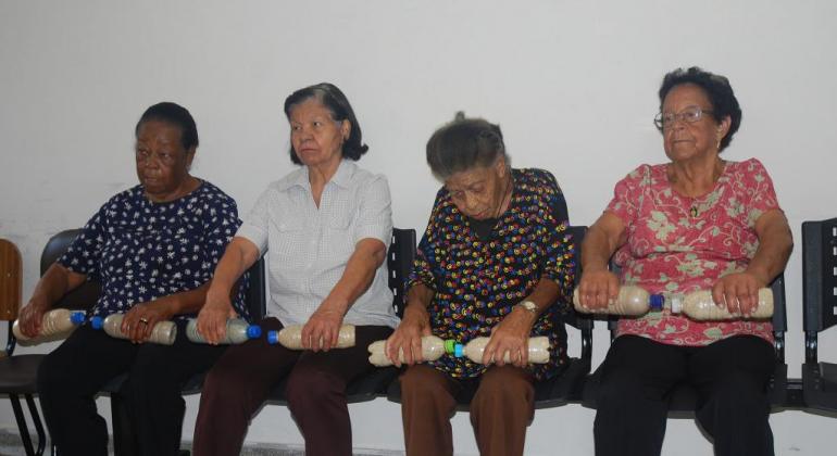 Quatro idosas segurando pesos durante atividade em grupo de prevenção de quedas.
