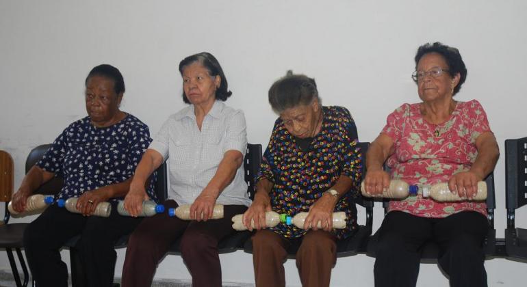Grupo de prevenção de quedas ajuda idosos a evitar acidentes domésticos. Foto: Melissa Reis/PBH Quatro idosas segurando pesos durante atividade em grupo de prevenção de quedas.