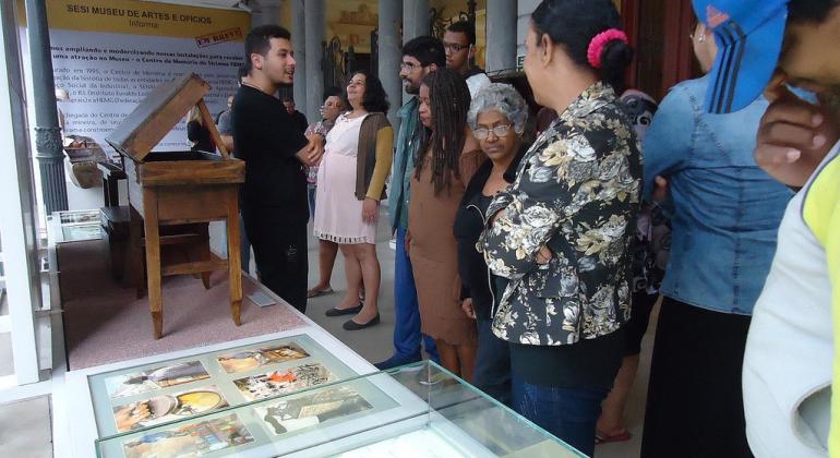 Cerca de quinze pessoas observando objetos em exposição no museu