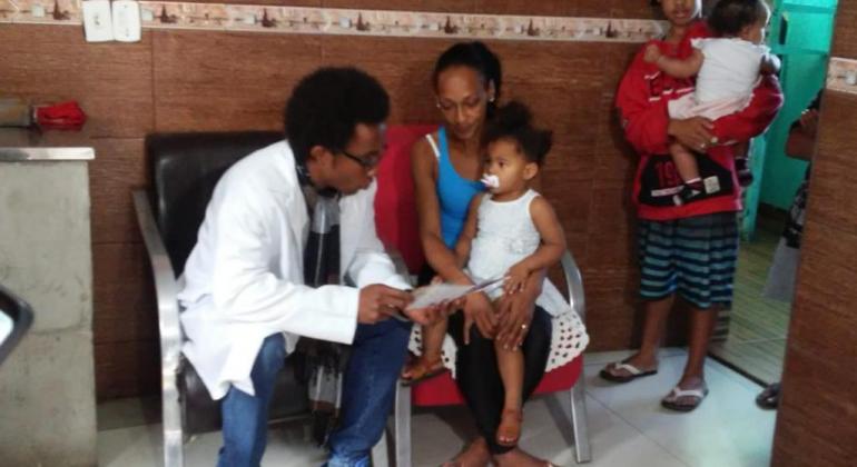 PBH intensifica vacinação contra sarampo e pólio em crianças com doses em atraso Agente de saúde sentado em cadeira, ao lado de uma mãe, também sentada, com uma criança no colo