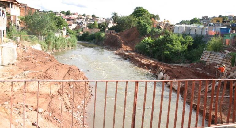 Foto feita de cima de uma ponte que passa sobre o Ribeirão do Onça. Nas margens do Ribeirão, há casas e áreas em obra.