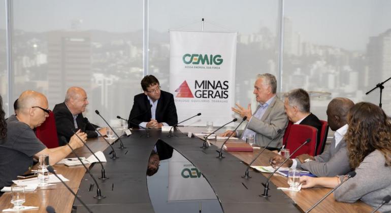 Sete membros da Prefeitura de BH, da Cemig e da Secretaria Estadual de Cultural sentados em torno de uma mesa. Ao fundo, um banner da Cemig e do Governo de Minas Gerais.