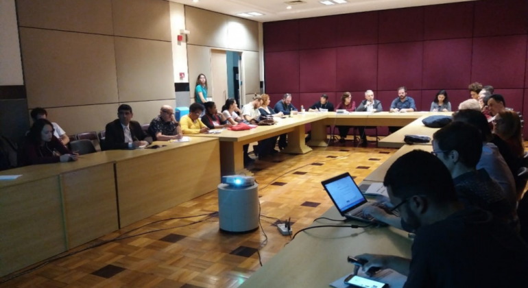 COMUC discute e aprova proposta orçamentária da Cultura para 2019 Sala fechada, com mesa em formato de U, tem cerca de 15 pessoas sentadas