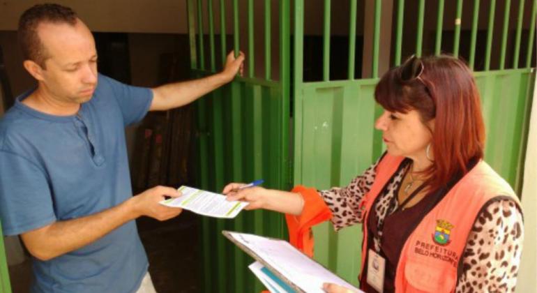 Entre os dias 16 e 18/7, profissionais da SLU fazem campanha educativa na rua Padre Pedro Pinto, 1055, no centro de Venda Nova. Foto: Divulgação PBH Técnica da SLU entrega panfleto a homem que está ao lado de um portão aberto