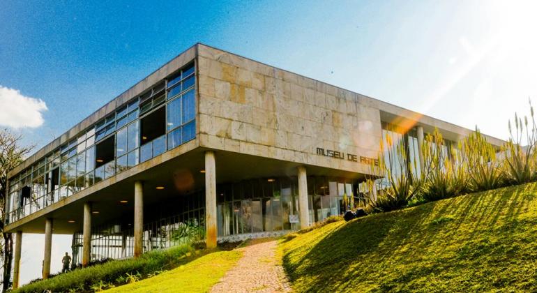 Foto do prédio do Museu de arte da Pampulha em dia de sol. Há um jardim à frente do prédio