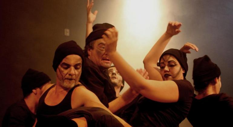 da Trupe de Teatro e Pesquisa. Foto: Yuri Simon Cinco atores vestidos de camisetas e gossors pretos dançam.