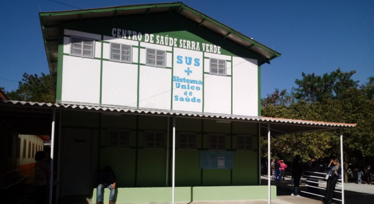 Fachada do Centro de Saúde Serra Verde, pintado em branco e verde, com os dizeres em azul "SUS - Sistema Único de Saúde"
