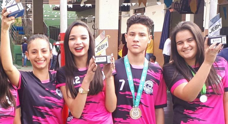 Quatro participantes dos Jogos Escolares de Belo Horizonte, três garotas e um garoto, exibem suas medalhas em sorriem. 