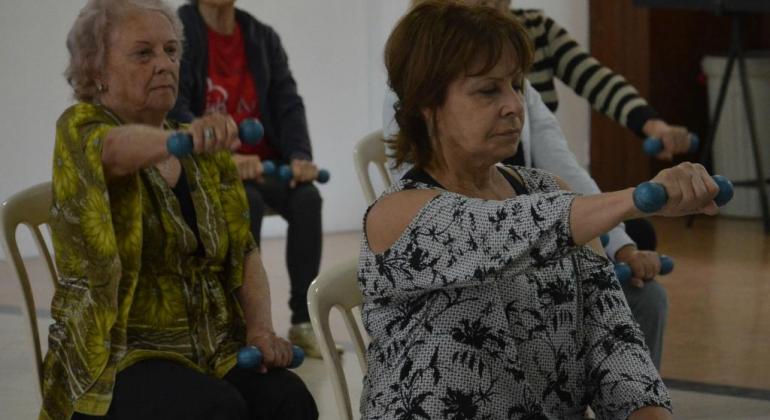 Vida Ativa faz atividades físicas e recreativas específicas para idosos. Foto: Marcelo Machado/PBH cinco idosas praticando exercícios físicos erguendo pesos