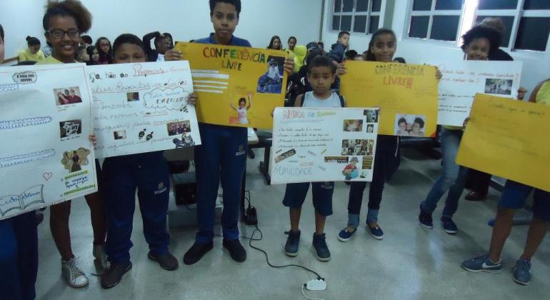 Oito crianças em sala cheia segurando cartazes sobre a conferência livre