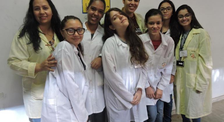 8 jovens alunos da Rede Municipal vestindo jaleco com logo do projeto de iniciação científica