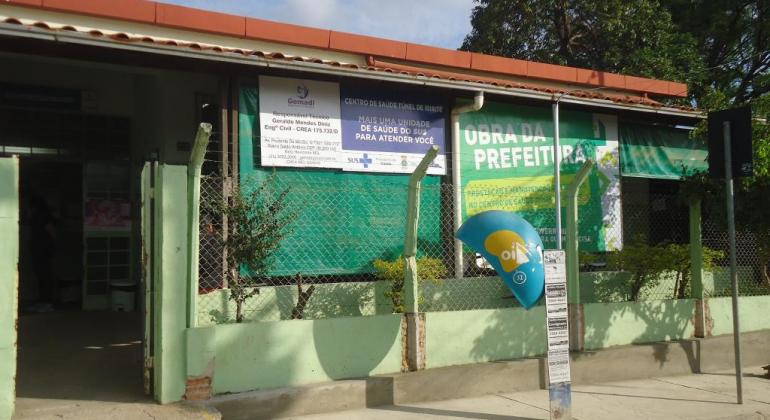 Fachada de centro de saúde, orelhão telefônico, banner informativo de Obra da Prefeitura