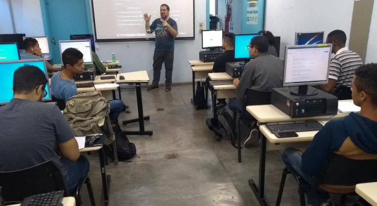 Professor e cerca de dez alunos em laboratório de computadores