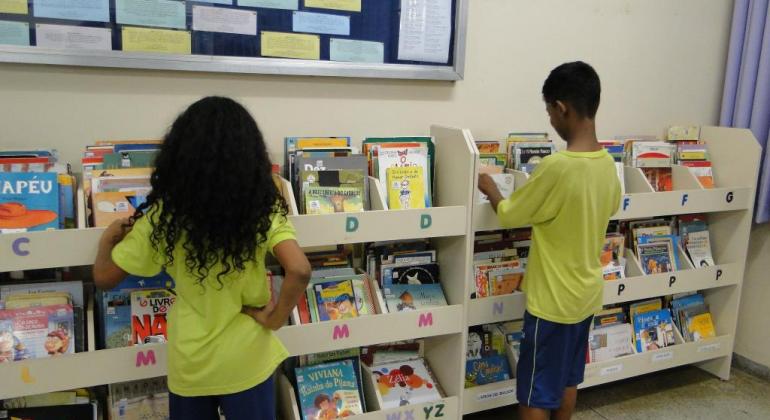 Duas crianças na biblioteca escolar escolhendo livros na prateleira