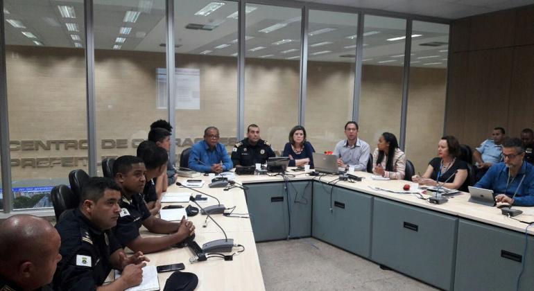 Cerca de quinze pessoas sentadas ao redor de grande bancada, entre policiais, outras autoridades e servidores no Centro de Operação da PBH.