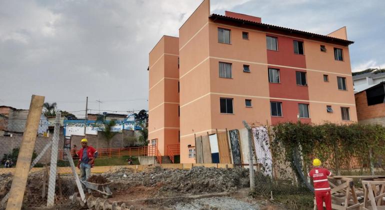 Moradores da Vila São João Batista comemoram retomada de obra do OP. Foto: Divulgação/PBH Dois funcionários da Prefeitura de BH trabalham em obras de urbanização ao lado de prédios.