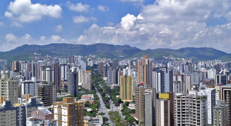 A foto mostra a vista de Belo Horizonte, do centro para a Serra do Curral, em um dia de céu claro com poucas nuvens.