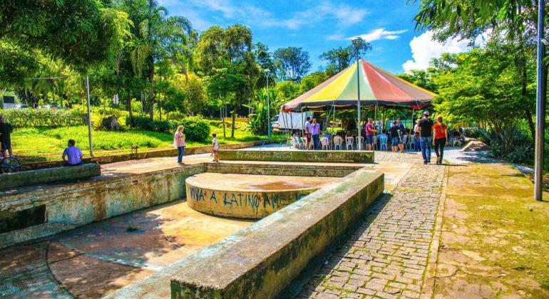 Parque Lagoa do nado em dia ensolarado. Na foto, há árvores e uma barraca colorida montada com pessoas em volta