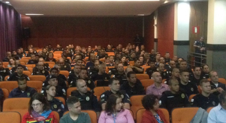 A foto mostra um auditório onde há cerca de 50 pessoas sentadas, entre elas agentes da guarda municipal.