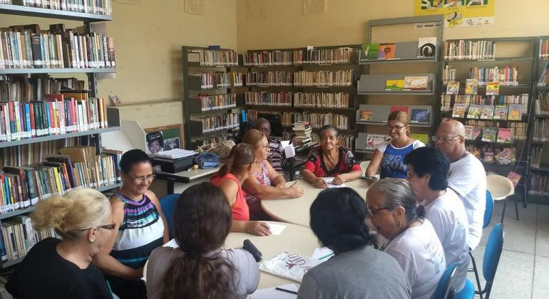 Grupo de cerca de dez idosos reunidos sentados em biblioteca 