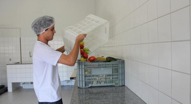 Funcionário do banco de alimentos despejando frutas e legumes de uma caixa à outra