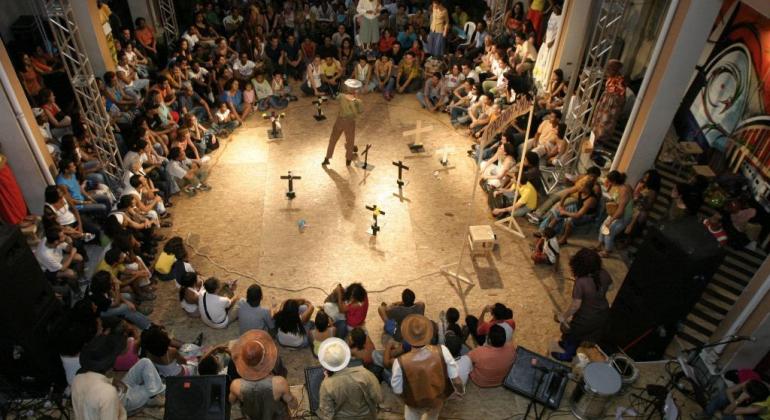 FMC abre inscrições para novas oficinas do Projeto Arena da Cultura Público sentado em circulo assiste artista no centro do palco