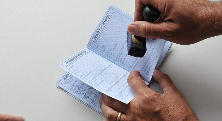 A foto mostra uma mão batendo um carimbo em uma carteira de trabalho.