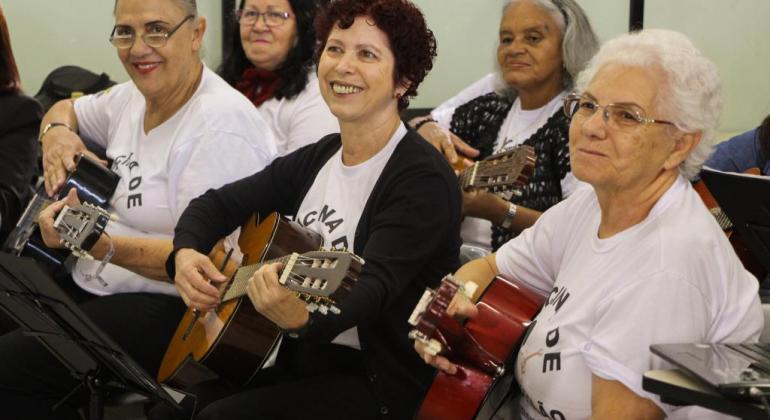 Cinco idosas sentadas seguram violões